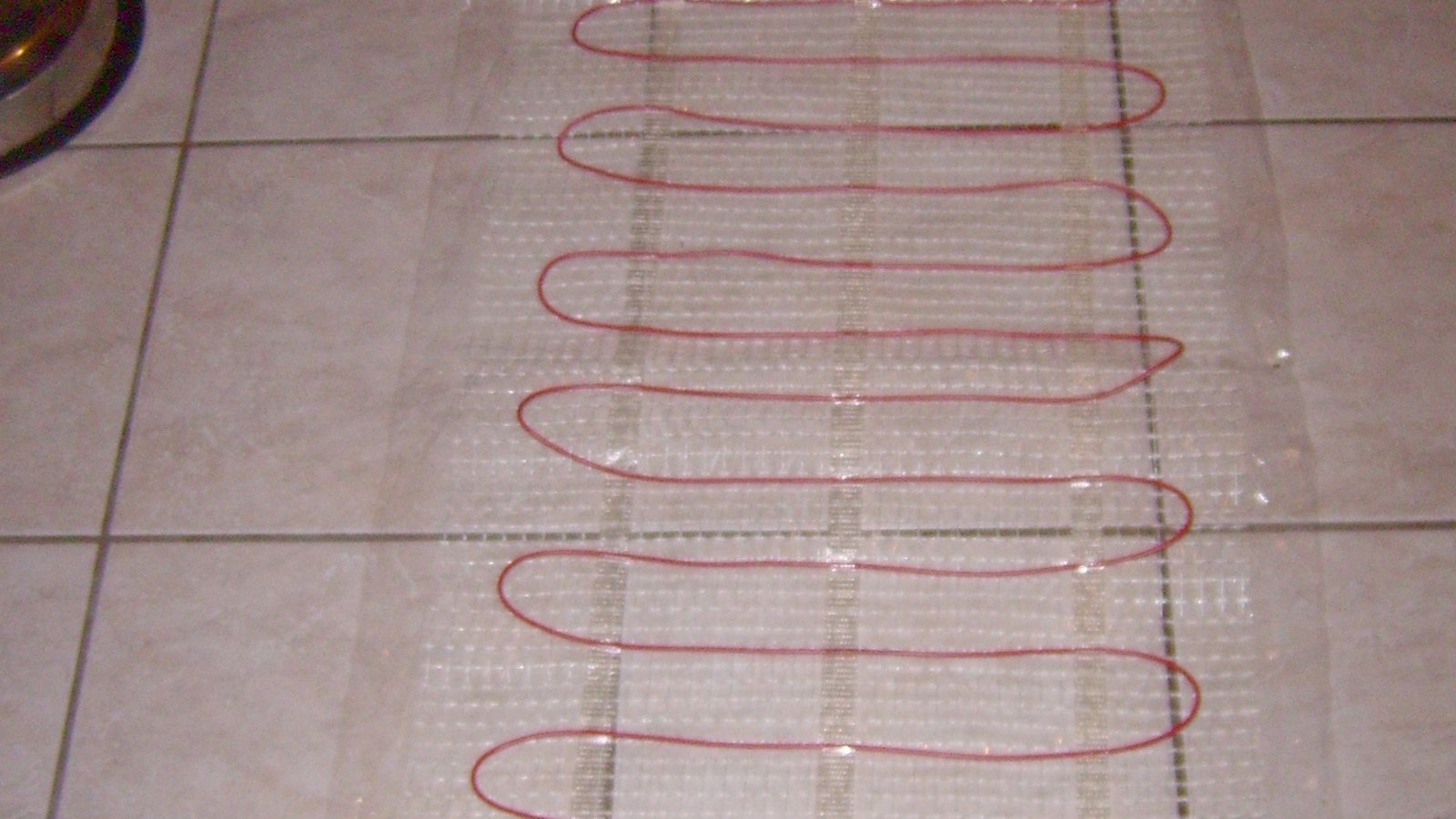 Fil chauffant rouge disposé en boucles régulières sur une trame avant la pose de carreaux